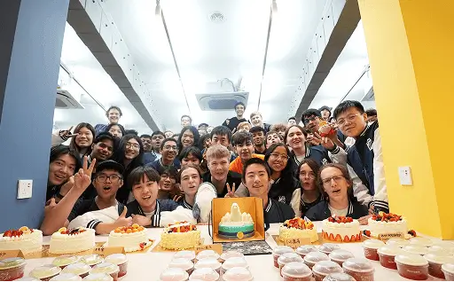 A crowd of Hack Clubbers smiling behind a table of cupcakes