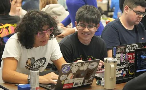 Teenagers coding on sticker-covered laptops at a Hack Club hackathon